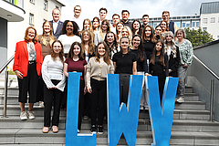 Die Nachwuchskräfte, die heute ihre Ausbildung bzw. ihr duales Studium beim LWV beginnen, mit LWV-Beigeordnetem Dieter Schütz (oberste Reihe links) und Ausbildungsleiterin Birgit Behr (2. Reihe links). (Foto: LWV-Öffentlichkeitsarbeit) Gruppenfoto von den 24 neuen Nachwuchskräften auf einer Treppe. Unterhalb vorne befinden sich die drei großen Buchstaben "LWV"