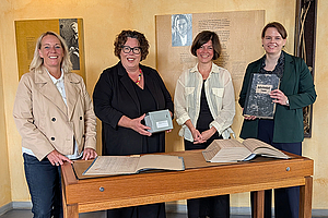 Gruppenfoto mit Susanne Schneider, Susanne Simmler, Dr. Ann Katrin Düben und Tamara Block hinter einem Tisch, auf dem alte Akten liegen. Letztere hält ein altes Buch in der Hand.