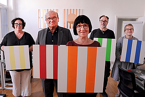 Der Klinikdirektor, die LWV-Landesdirektorin, die Ergotherapeutinnen und ein weiterer Mann halten lachend die gestreiften Bilder in die Kamera.