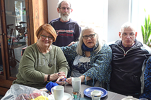 Zwei Frauen und ein Mann sitzen an einer Kaffeetafel im Oikos-Sozialzentrum, hinter ihnen steht ein weiterer Mann