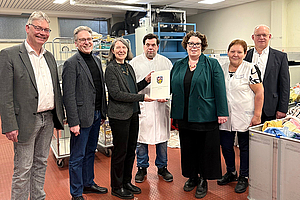 Gruppenfoto von der Bescheidübergabe vor der Faltmaschine