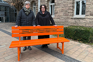 Susanne Simmler und Martina Maurer stehen hinter der orangenen Sitzbank